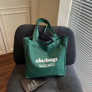 Borsa tote minimalista in tela verde scuro con stampa di lettere su sedia grigia