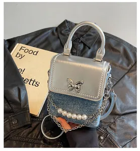 Dettaglio borsa in pelle argento con chiusura a farfalla e decorazioni in perle e denim