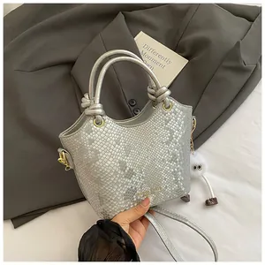 Détail du sac à main argenté à motif serpent avec poignée nouée et anneaux dorés