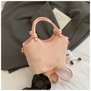 Détail d'un sac seau rose à motif serpent avec pendentif peluche et logo doré chic
