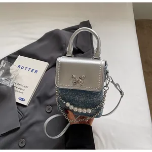 Dettaglio della piccola borsa a tracolla in denim con fibbia a farfalla e catena di perle