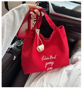 Détail du sac cabas en toile rouge avec broderie et accessoire en cuir beige
