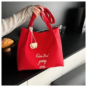 Détail du cabas en toile rouge avec broderie blanche et accessoire en cuir beige