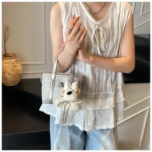 Detail of silver mini tote bag with snakeskin texture and plush bear charm decoration