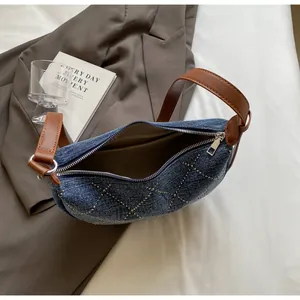 Dettaglio borsa a tracolla in denim blu con borchie argentate e tracolla in pelle marrone
