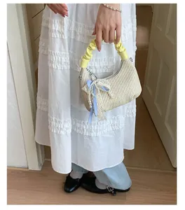 Dettaglio borsa a nuvola intrecciata con fiocco a quadri blu, perle e manico giallo