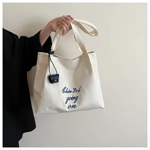 Détail du sac cabas en toile avec broderie bleue et petit pendentif en cuir bleu