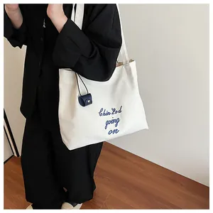 Vue détaillée du sac cabas en toile blanche avec broderie bleue et petite pochette marine