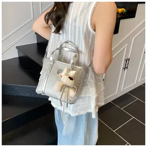 Silver metallic bucket bag with fluffy charm shown as a stylish crossbody on a model