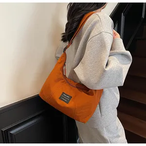 Dettaglio della borsa a tracolla in nylon arancione con toppa nera indossata da una modella
