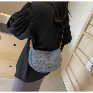 Dettaglio della borsa a sella in denim azzurro con borchie e tracolla in pelle