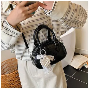 Close-up of black glossy textured mini bag with white lace bow and pearl heart charm