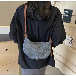 Dettaglio borsa a luna in denim blu con strass e tracolla in pelle marrone regolabile