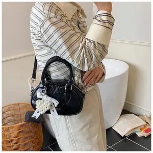 Detail of black patent leather mini bag with heart pearl charm and white silk bow