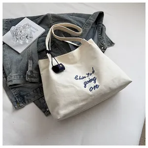 Détail du sac cabas en toile blanc cassé avec broderie bleue et étiquette en cuir sur l'anse