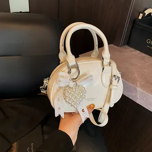 Creamy white bowler handbag with pearl heart charm and lace bow on a dark background