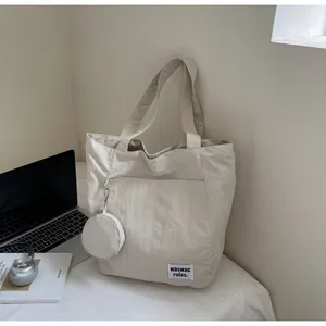 Détail du grand sac cabas crème avec petite pochette ronde sur un lit avec accessoires