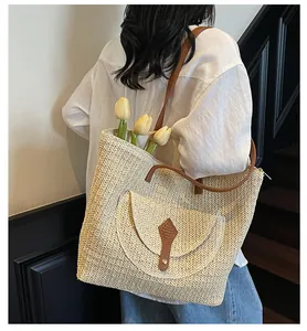 Detail view of woven straw tote bag featuring brown leather straps and front flap pocket
