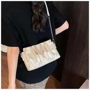 Detail of a creamy white pleated cloud bag with silver metal chain on a female model