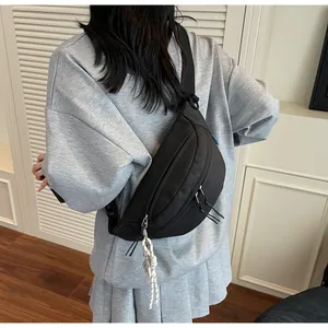 Detail view of black nylon chest bag with dual zippers and rope pendant on model back