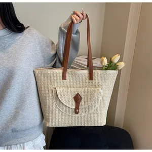 Straw tote bag with brown leather handles and front pocket shown in lifestyle setting