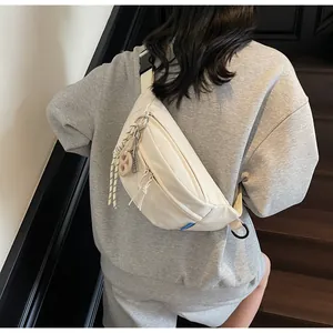 Rear view of cream canvas crossbody bag with adjustable strap and braided charm on a model