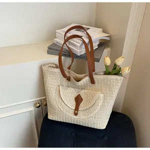 Detail of minimalist straw tote bag featuring brown leather straps and zip closure
