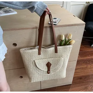 Detail view of woven straw tote bag featuring herringbone texture and brown leather handles