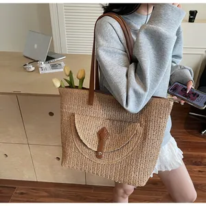 Detail of hand-woven straw tote bag featuring brown leather straps and metallic buckle