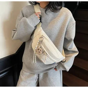 Detail of off-white canvas sling bag featuring a pretzel pendant and wide shoulder strap