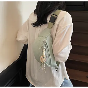 Close-up of mint green canvas crossbody bag with adjustable strap and decorative charm