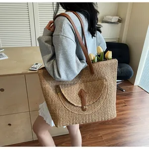 Detail of spacious straw tote bag with brown leather straps and decorative buckle flap
