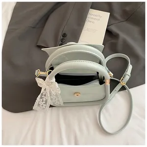 Detail of mint green handbag featuring lace bow charm and adjustable strap on bed