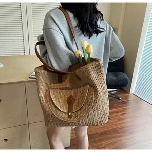 Detail shot of woven straw tote bag with brown leather straps and front buckle pocket