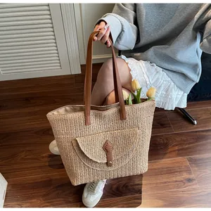 Detail of handwoven straw tote bag with brown leather handles and a decorative front pocket