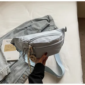Detail view of a light blue canvas chest bag with zipper pockets on casual denim background