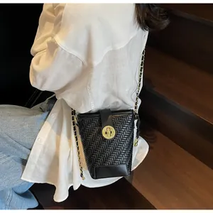 Détail du sac seau noir en cuir tressé avec boucle dorée et bandoulière en chaîne