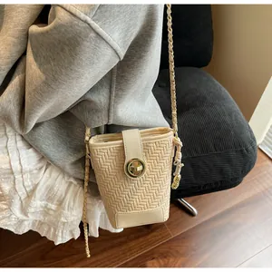 Gros plan d'un sac seau tissé beige avec boucle dorée et bandoulière en chaîne