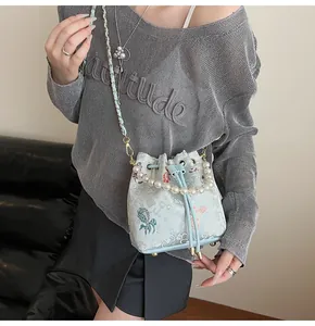 Detail of light blue bucket bag with jacquard fabric, pearl handle and metal chain strap