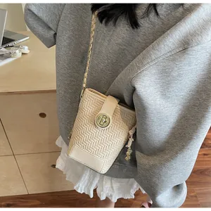 Détail d'un sac bandoulière beige tissé avec pendentif cacahuète et bandoulière dorée