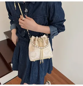 Close-up of cream drawstring bucket bag with gold butterfly prints and pearl handle details