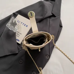 Sac seau beige tressé avec bandoulière chaîne dorée posé sur une veste grise