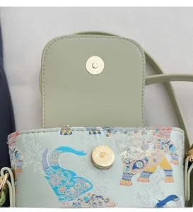 Close-up of golden magnetic buckle on mint green mini crossbody bag with elephant patterns