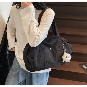Close-up of black nylon tote bag with a white plush charm shown on a model