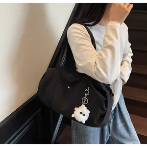 Detail of black nylon tote bag featuring a white plush monster keychain on shoulder strap