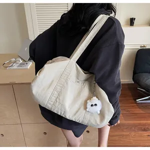 Detail view of a beige nylon tote bag with functional side pockets and a plush monster charm
