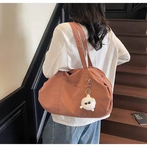 Close-up of brick red nylon tote bag with white plush monster charm and front pocket