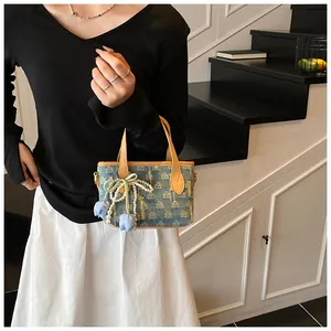 Dettaglio borsa di jeans con manici in pelle, fiocco di perle e ciondoli a fiori su gonna bianca
