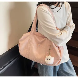 Pink nylon shoulder bag with front pocket and plush charm shown on a casual model