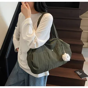 Detail of dark olive green nylon tote bag with white plush ball charm on model